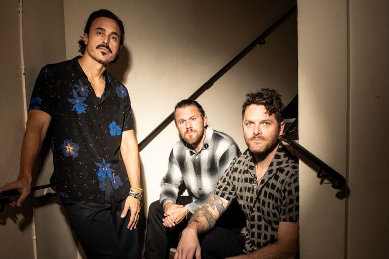 American rock band The Fray three members posing together on a dimly lit stairwell in a dramatic promotional portrait for SEO optimization.